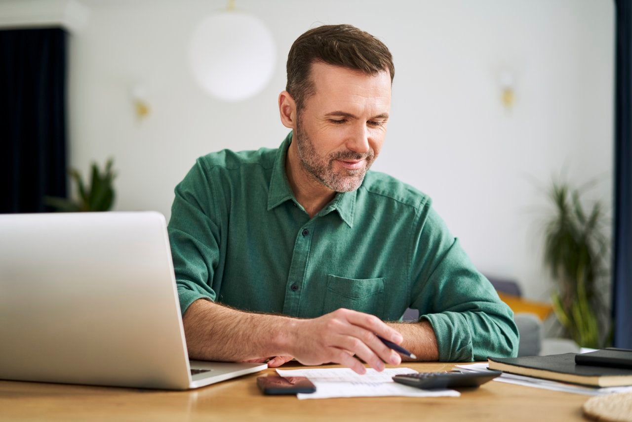 Man at home sitting with laptop and documents examining home finances