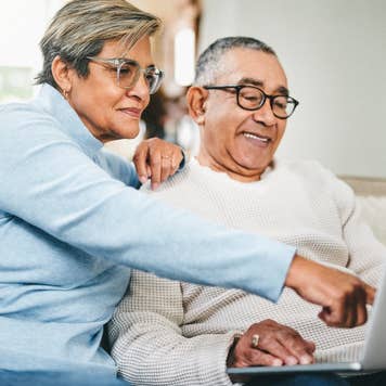 Older couple on a couch, smiling, looking at a laptop