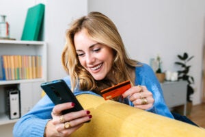Happy woman holds credit card while looking at her phone