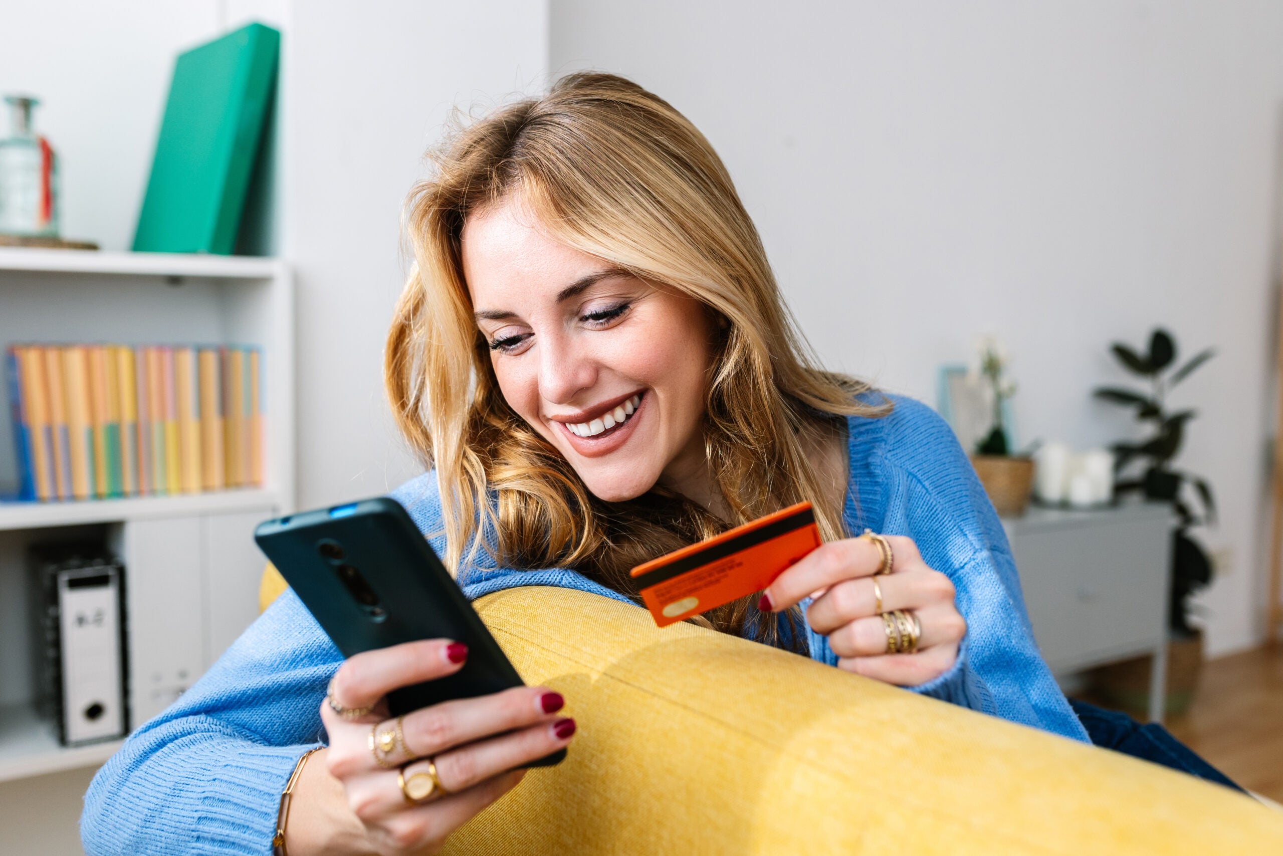 Happy woman holds credit card while looking at her phone