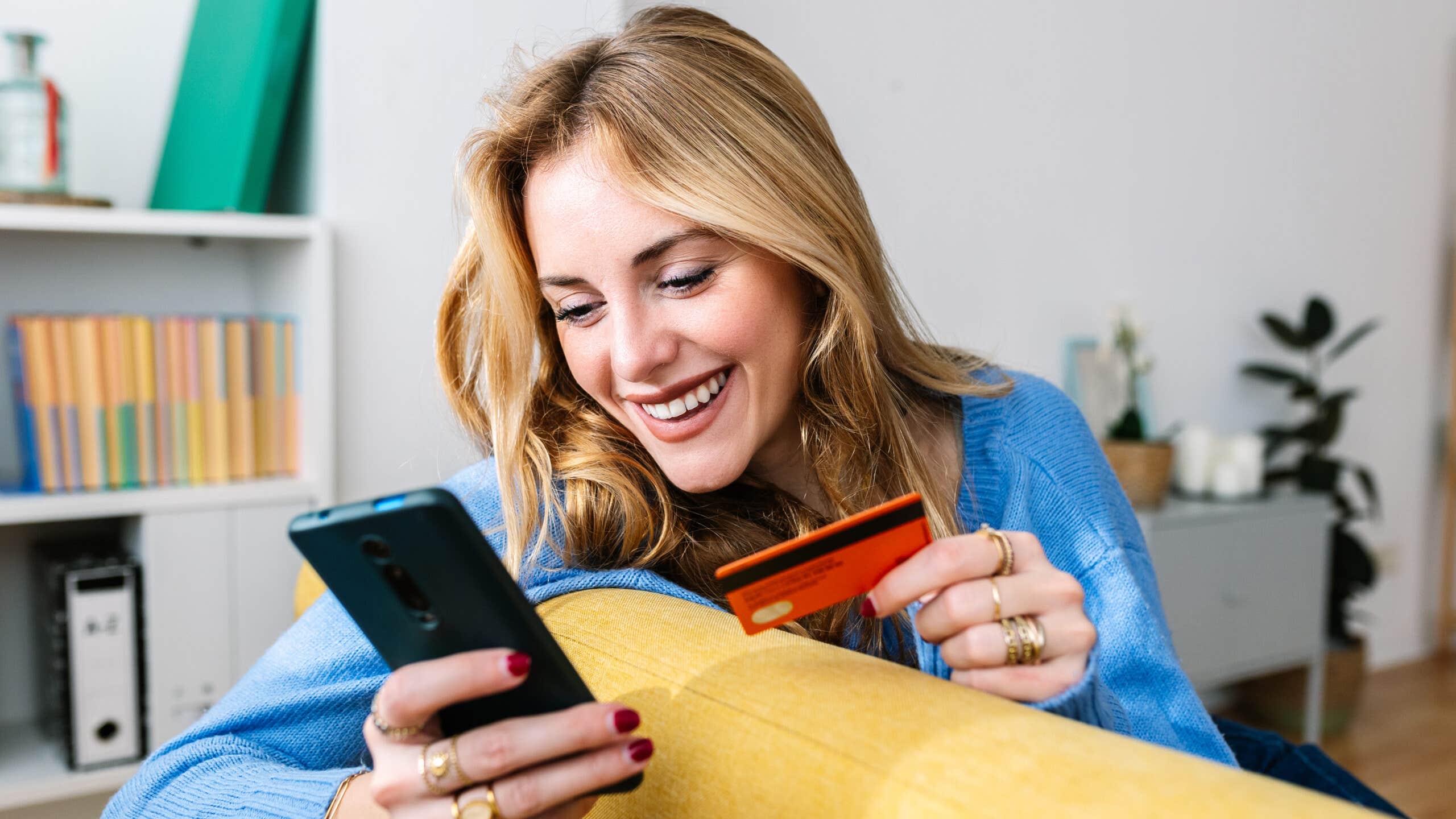 Happy woman holds credit card while looking at her phone