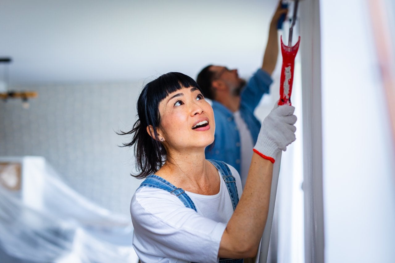 Happy couple renovating their home, painting the wall and smiling while working together