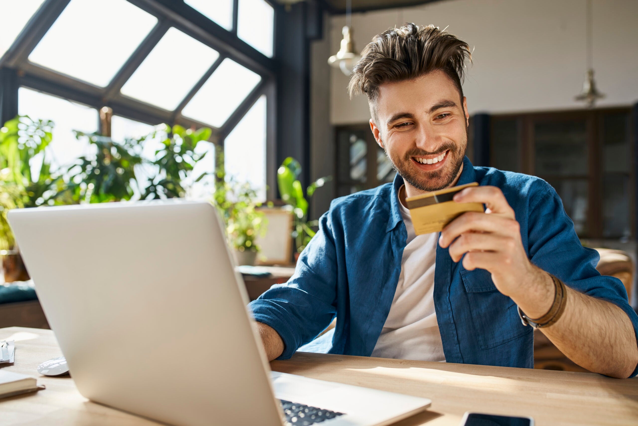 Man sits in front of laptop holding credit card and smiling