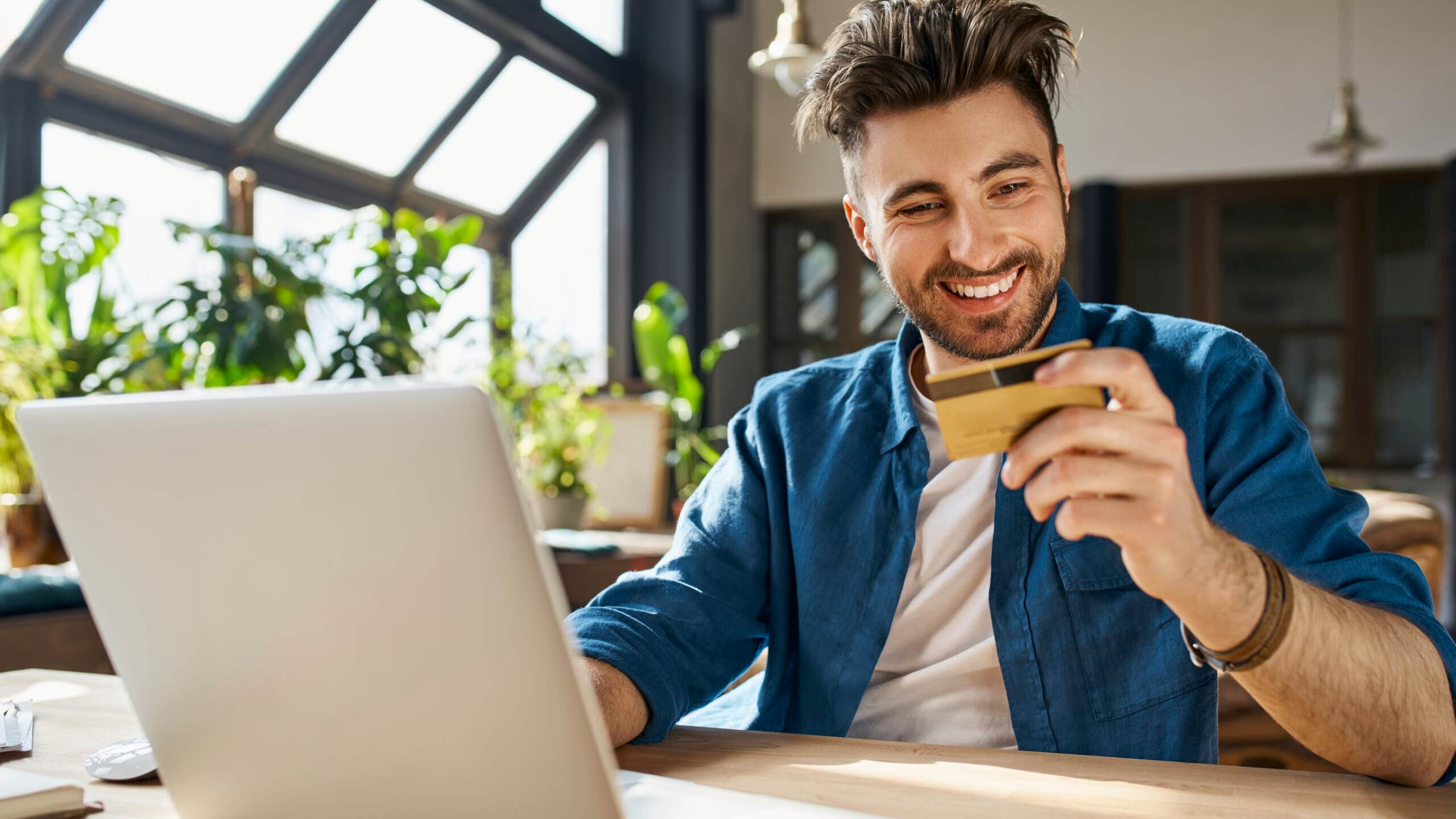 Man sits in front of laptop holding credit card and smiling