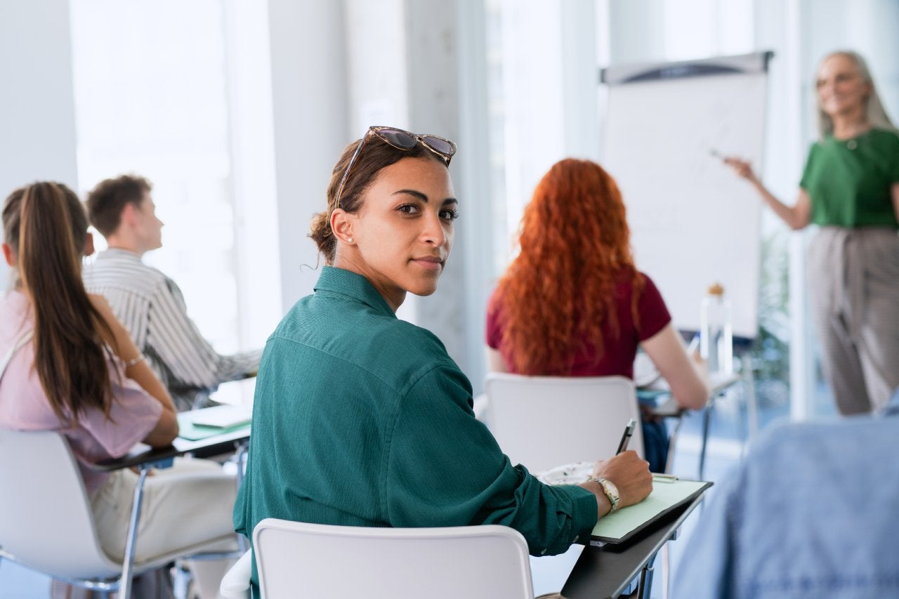 Portrait of young university student sitting in classroom indoors, looking at camera.
