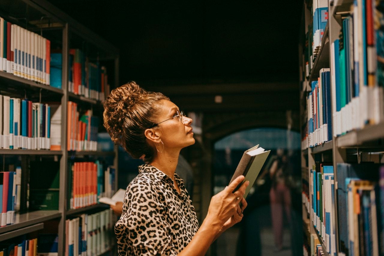 Female university student choosing book from shelf in library
