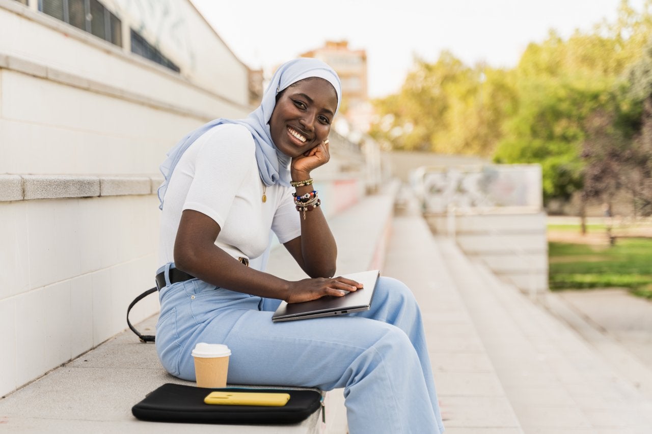 Portrait of African Student Girl wearing muslim hijab sitting on University staircase smiling at camera