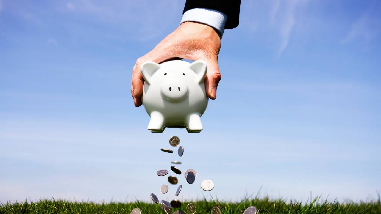 Hand holding a piggy bank with coins falling out of the bottom.