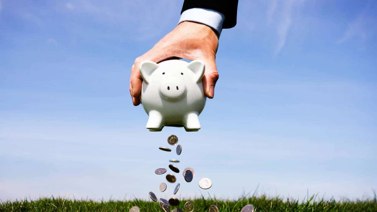 Hand holding a piggy bank with coins falling out of the bottom.