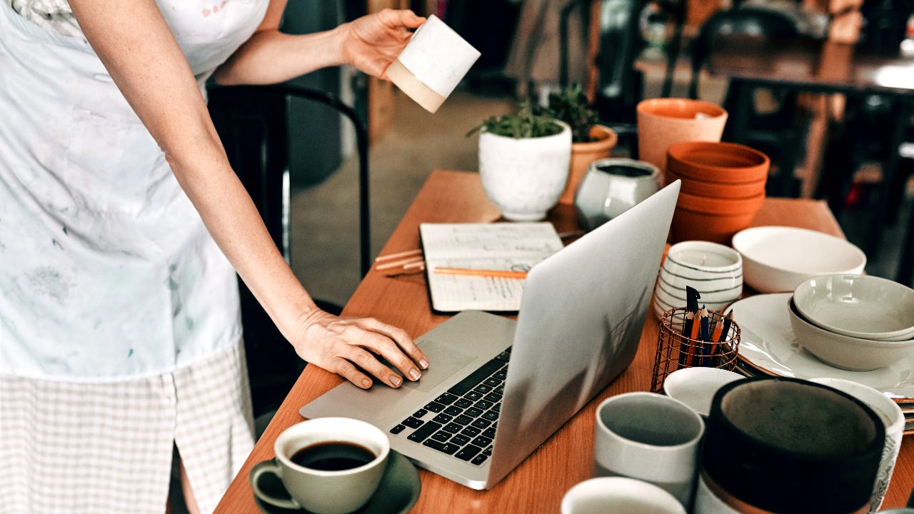 Cropped shot of a woman standing and using her laptop in her pottery workshop