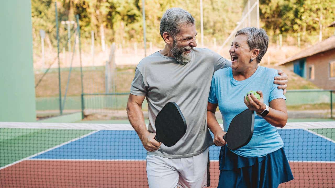 A senior couple walks away from a pickleball net with paddles in hand.