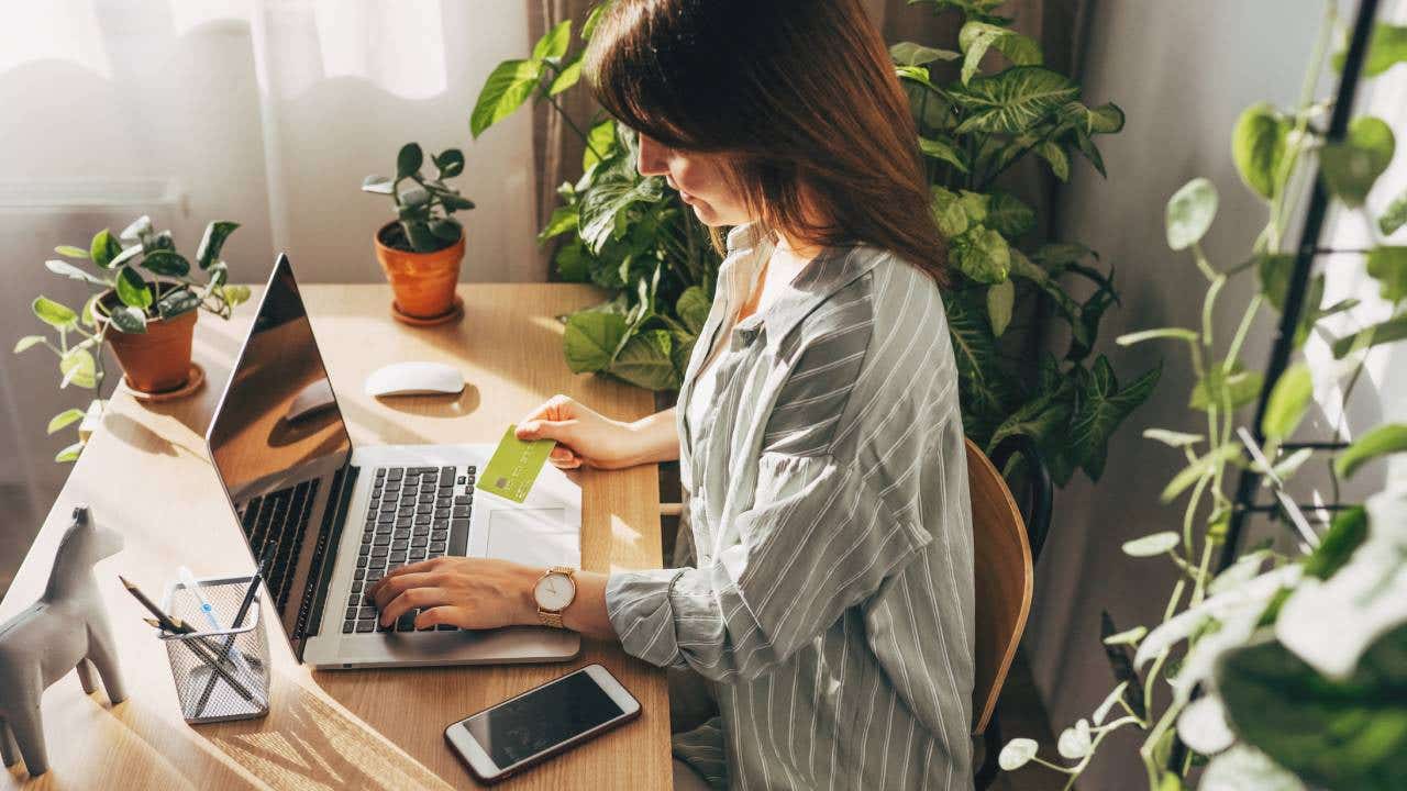Young woman holding credit card and using laptop computer.