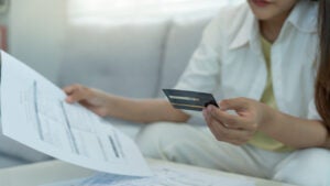 A woman holding a credit card with bills in front of her