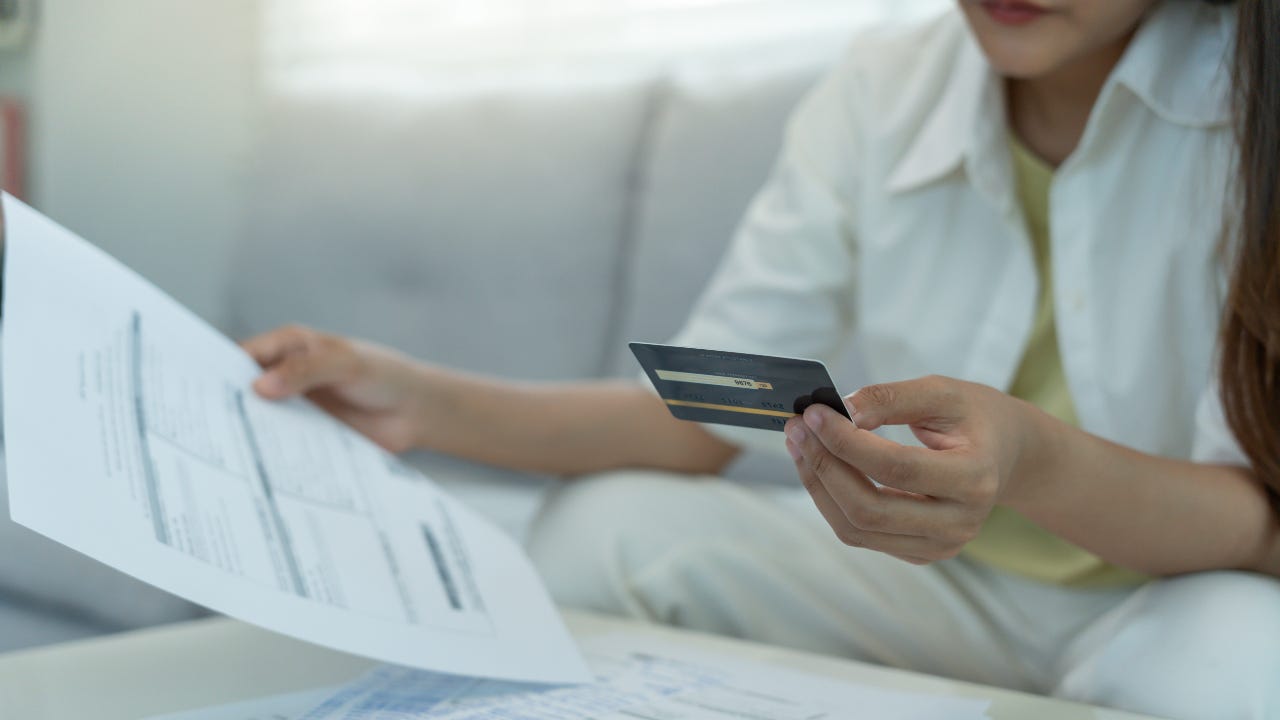 A woman holding a credit card with bills in front of her