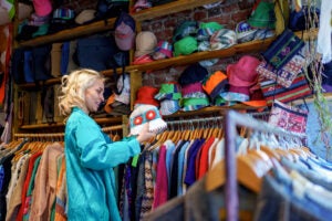 A woman browses through clothing racks filled with second-hand and vintage garments in a store.