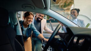 A white woman and a Black man view a car together while a Black saleswoman assists.