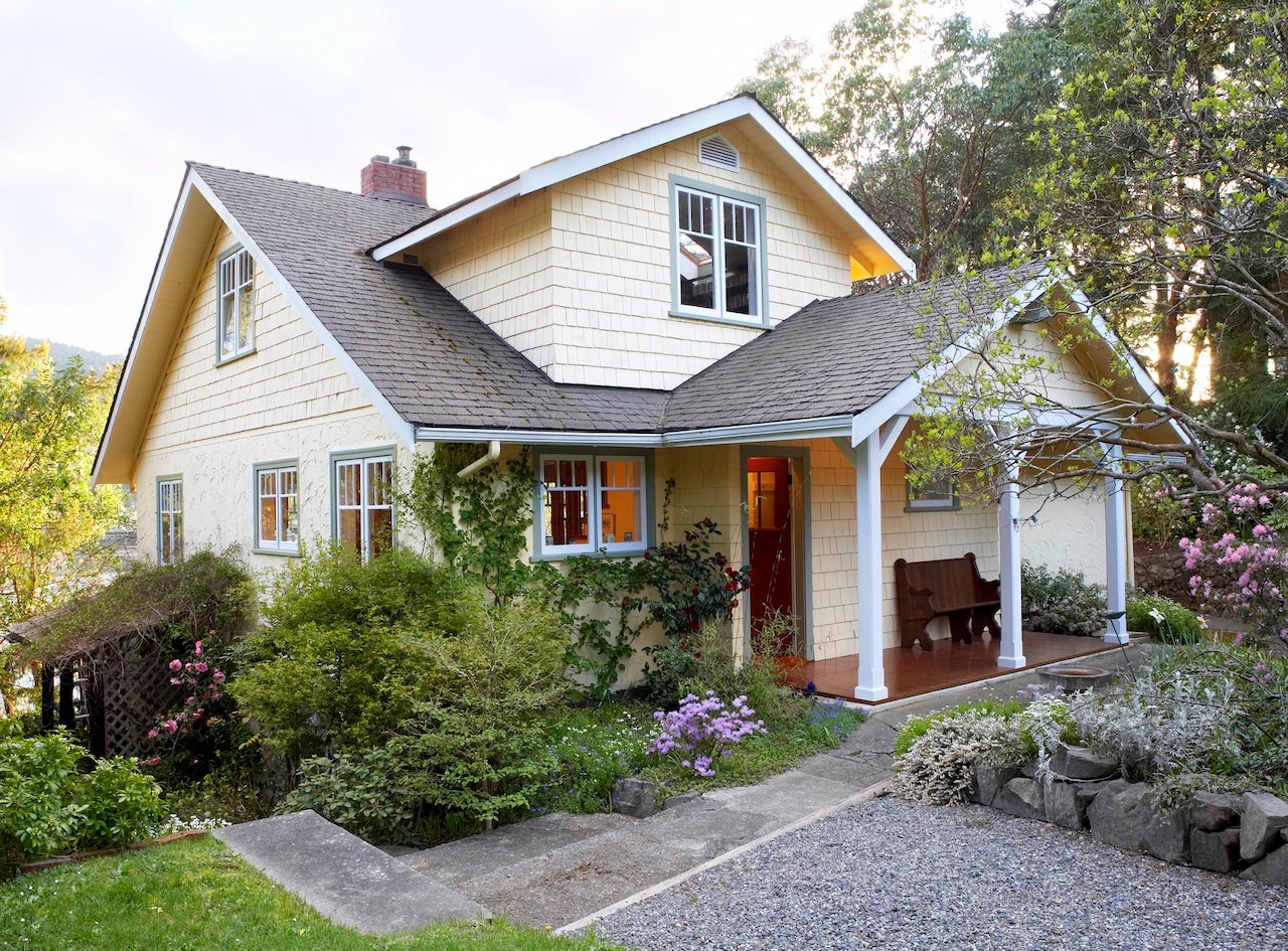 exterior of pale yellow cottage with flowering landscape and front porch