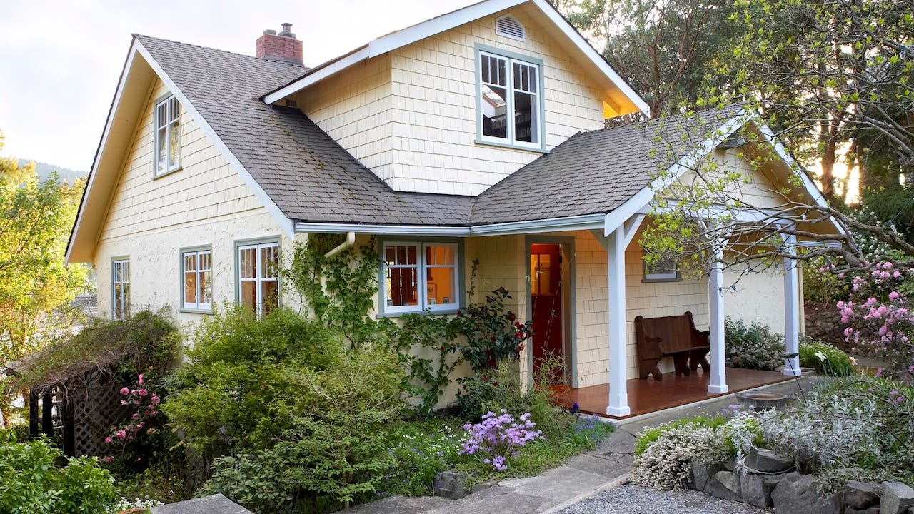 exterior of pale yellow cottage with flowering landscape and front porch
