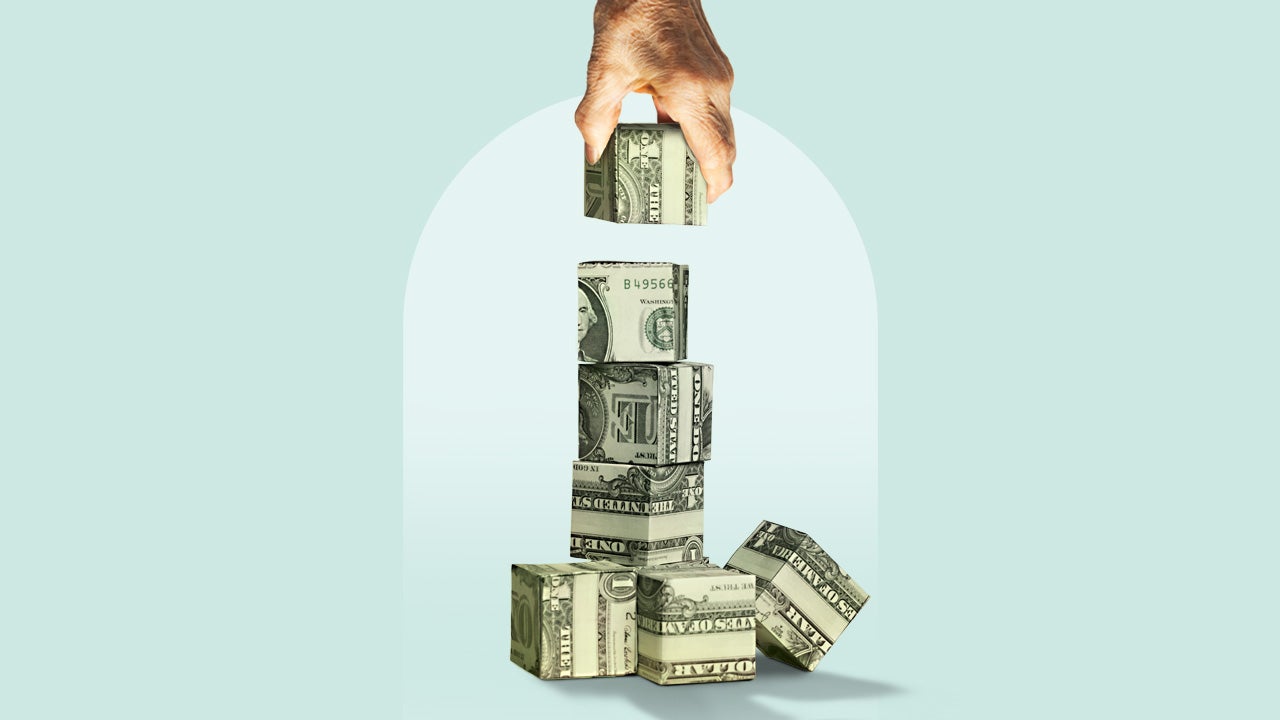 A hand stacks blocks made from folded dollars.