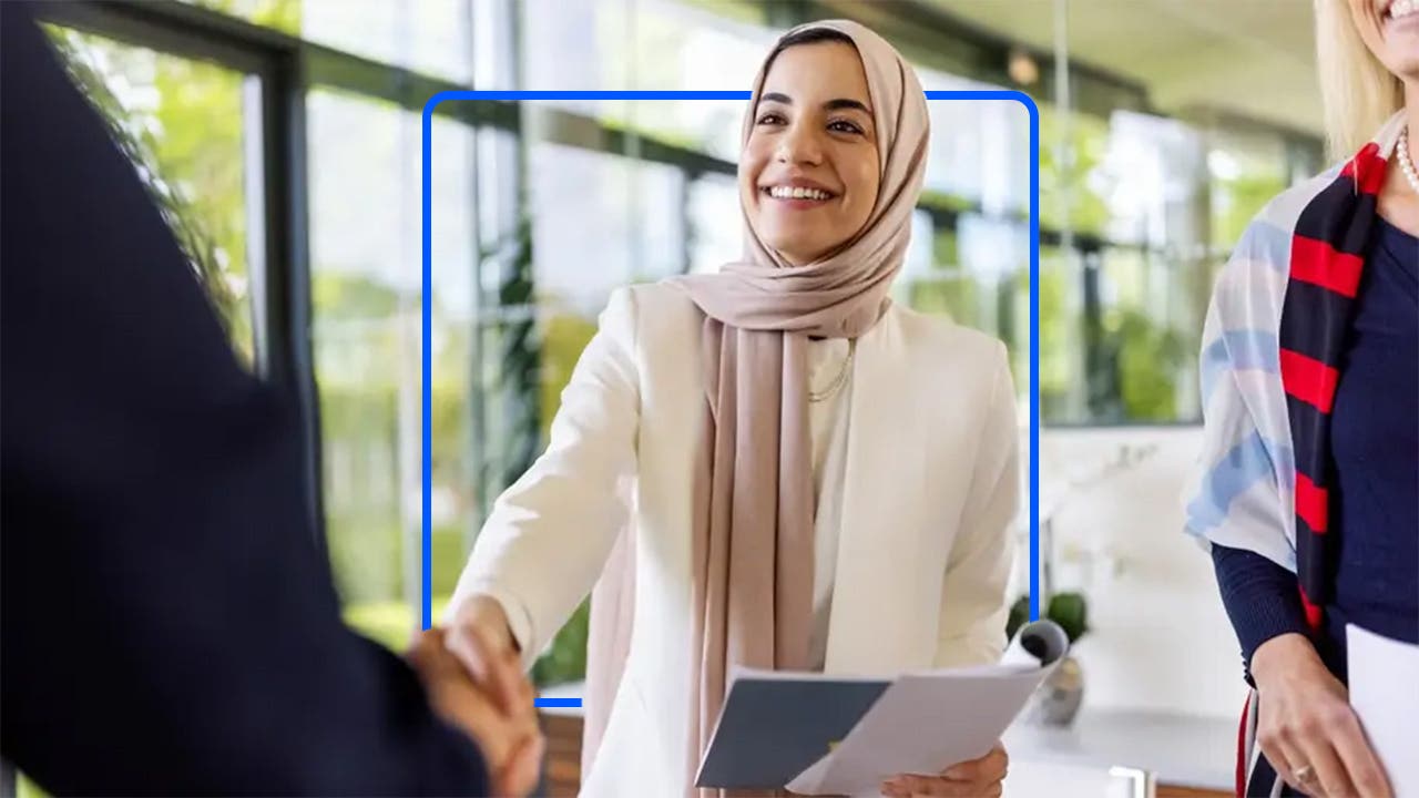 Woman shakes a hand during a job interview with a blue illustrated square.