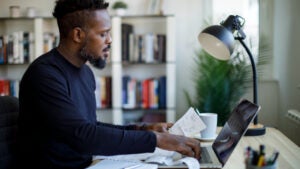 Thoughtful middle aged Black man reviews his finances at home using a laptop.