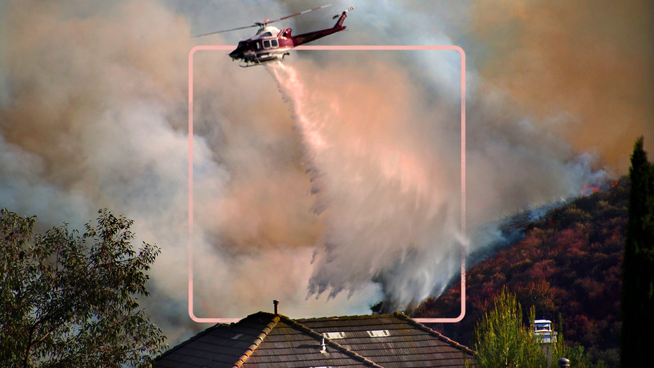 helicopter flying above wildfire in smoke-filled sky spraying water
