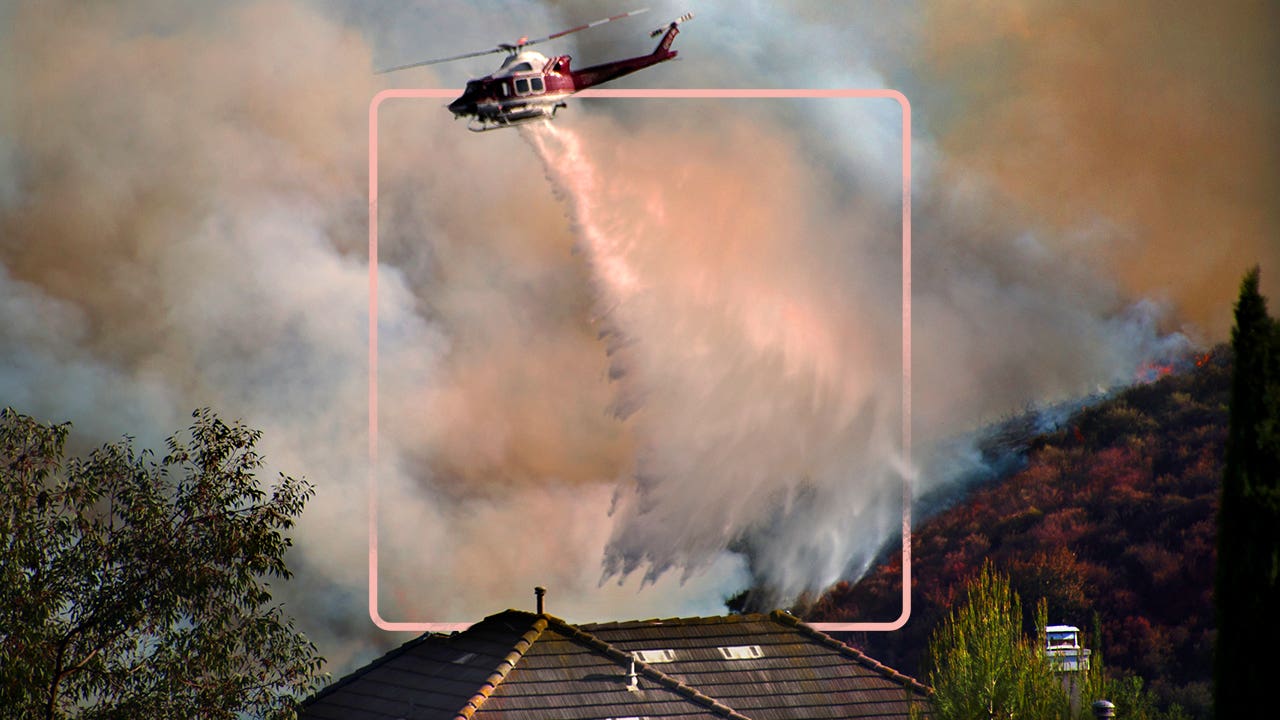 helicopter flying above wildfire in smoke-filled sky spraying water