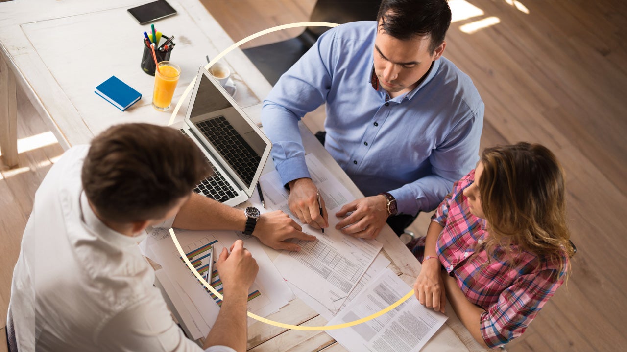 A couple sits across a desk from a banker, reviewing financial documents