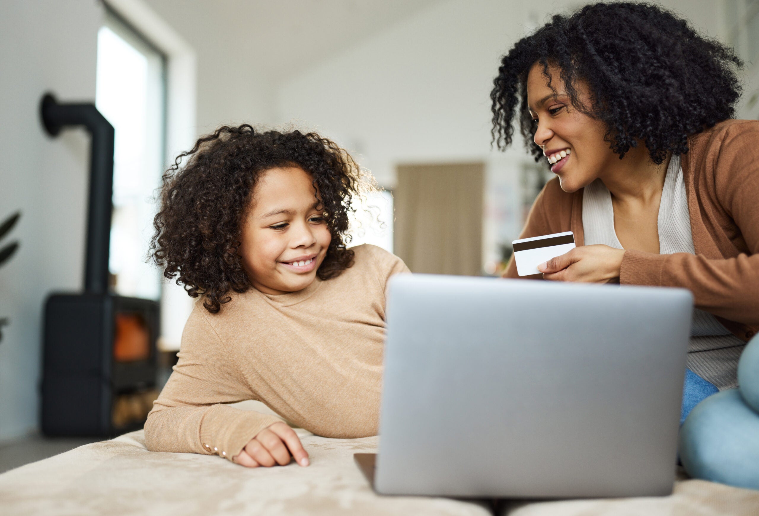 Happy African American single mother and daughter using credit card while shopping online over laptop at home.