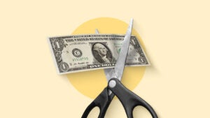 Image of a pair of open scissors with a U.S. dollar bill lying between the blades ready to be cut.