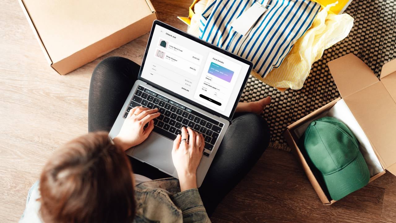 Young woman doing online shopping with laptop sitting on the floor at home