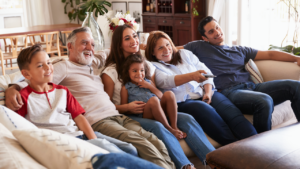 Three generation Hispanic family sitting on the sofa watching TV, grandmother using remote control