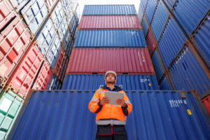 A dock worker examines imported goods in shipping containers.