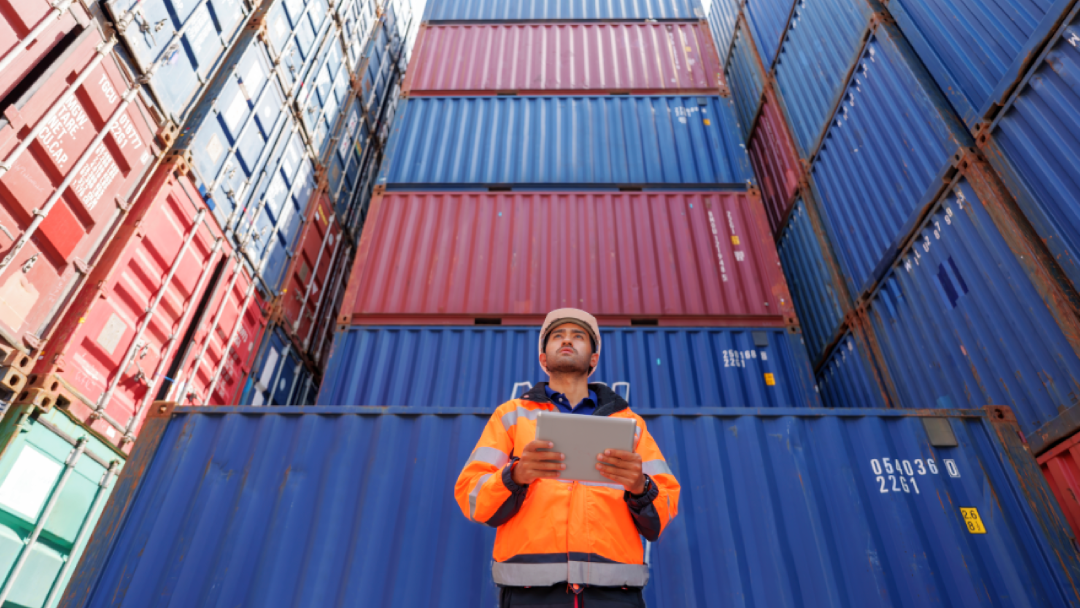 A dock worker examines imported goods in shipping containers.