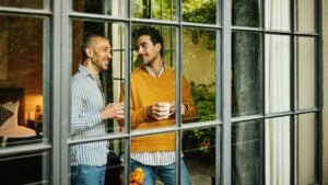 Medium wide shot view through window of smiling couple looking out of a bedroom