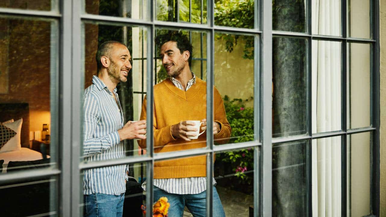 Medium wide shot view through window of smiling couple looking out of a bedroom