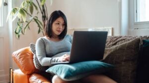 A woman sits on her couch and studies from her laptop.