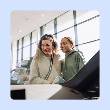 A smiling woman and her daughter look in at a car. There is an illustrated blue background.