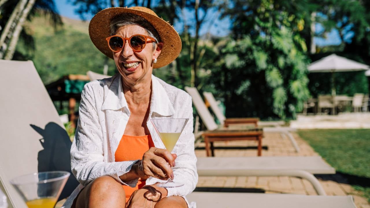 Portrait of a smiling mature woman, holding a drink, looking at camera and smiling near a poo