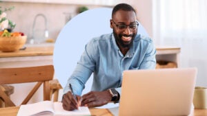 Black man happily sitting in front of laptop writing on document