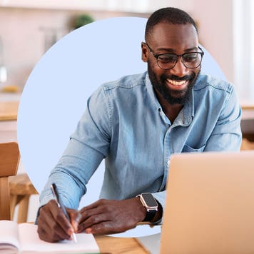 Black man happily sitting in front of laptop writing on document