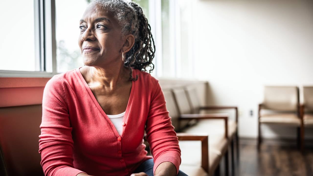 An older woman sits in a chair and looks out a window.