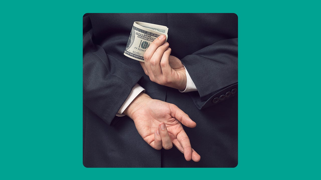 A person with their hands behind their back, with their right hand holding cash while their other hand has crossed fingers.