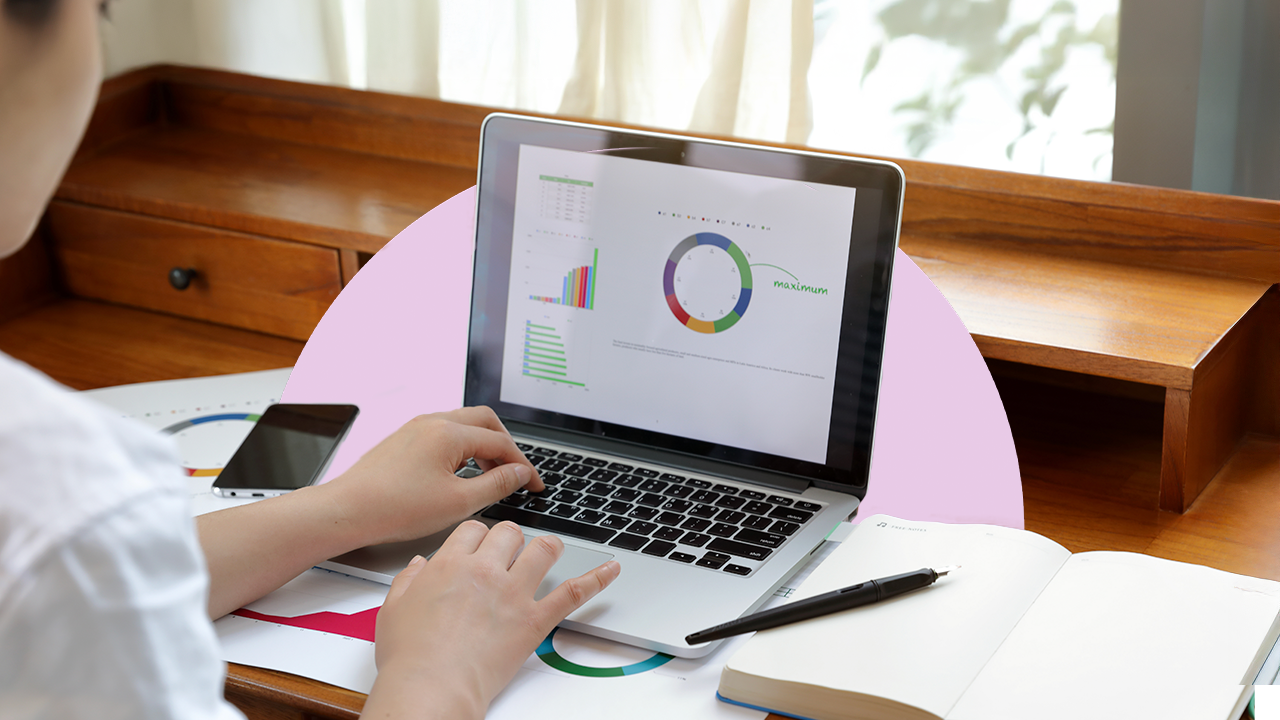 Woman sitting at a desk looking at a laptop with charts and graphs on the screen.