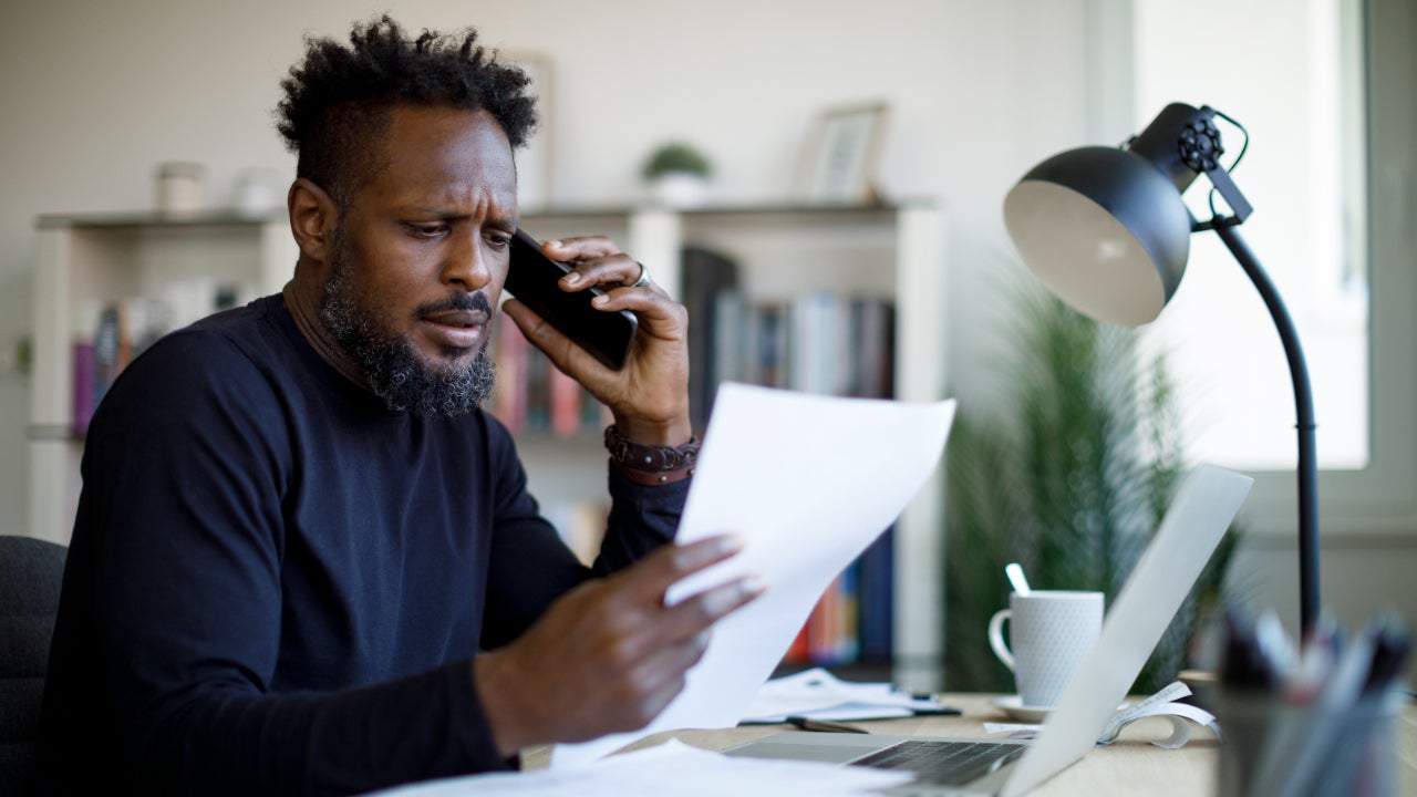 A Black man on the phone reviewing a paper with a thoughtful expression.