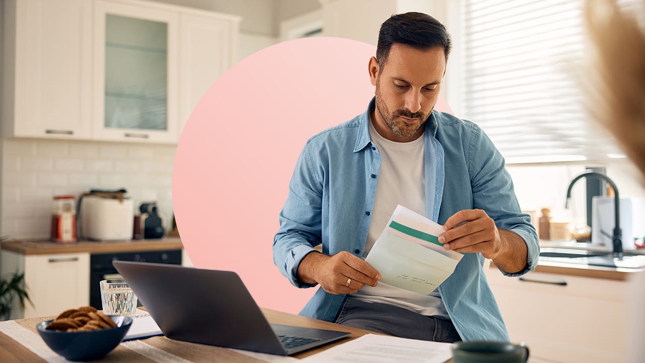 design image of a man looking at a piece of paper while on his laptop