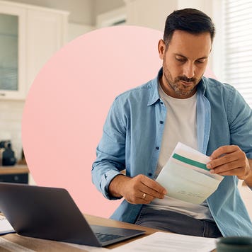 design image of a man looking at a piece of paper while on his laptop