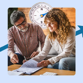 Older man with glasses sits on a couch next to a younger woman with curly hair. They are looking at official paperwork on a coffee table that also contains a calculator. There is an image of a large compass behind their heads and an blue arrow pointing from lower left to upper right.