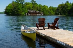 Wooden dock on a lake with two chairs and a canoe docked next to them.