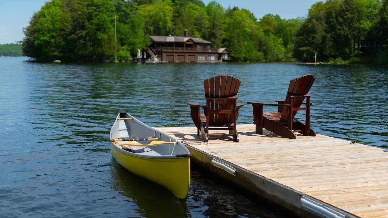 Wooden dock on a lake with two chairs and a canoe docked next to them.